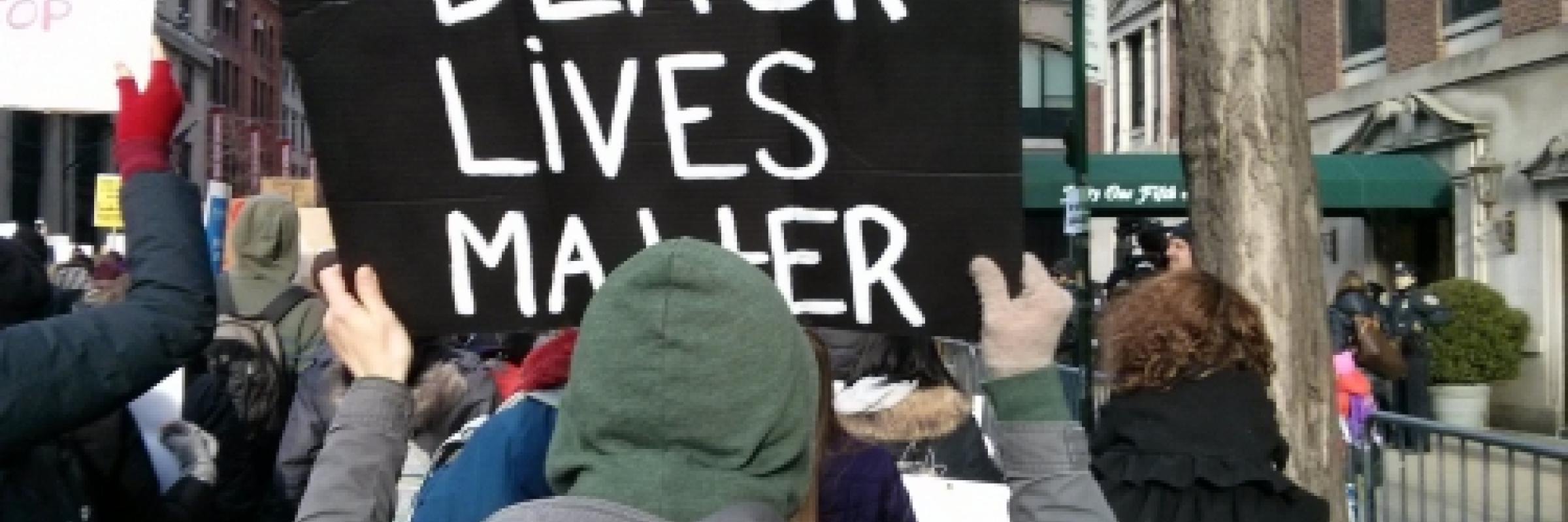 A crowd of people, with some holding placards - one being a 'black lives matter' placard