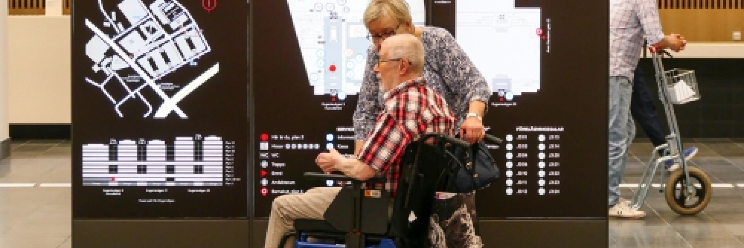 Image of a man in a wheelchair in front of a sign inside a building.