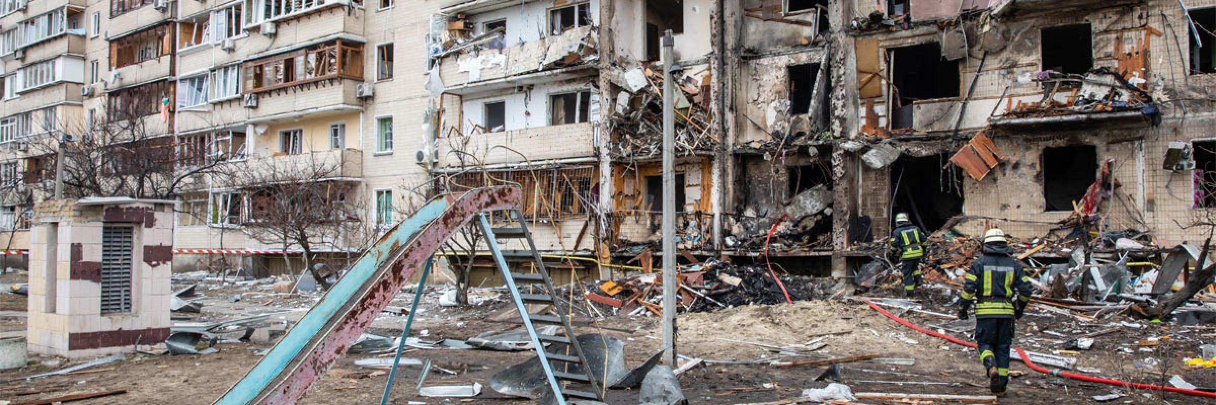 Image of a damaged building with firemen in front of it amidst debris