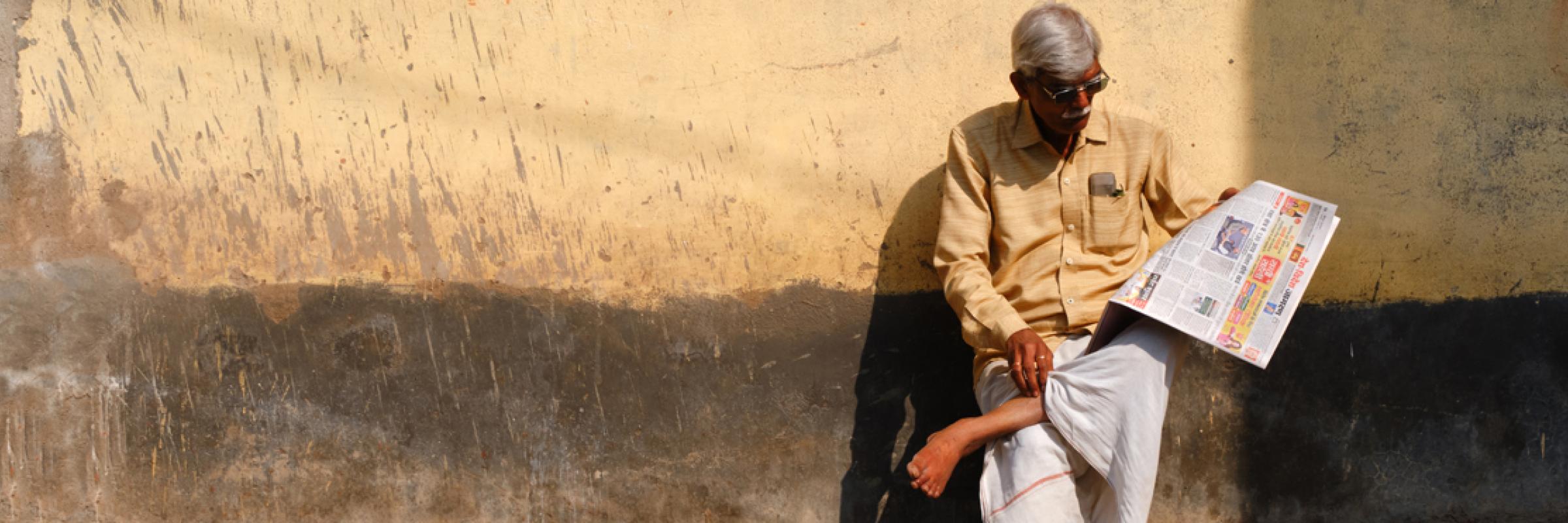 A person sitting on the side of a road reading a newspaper.