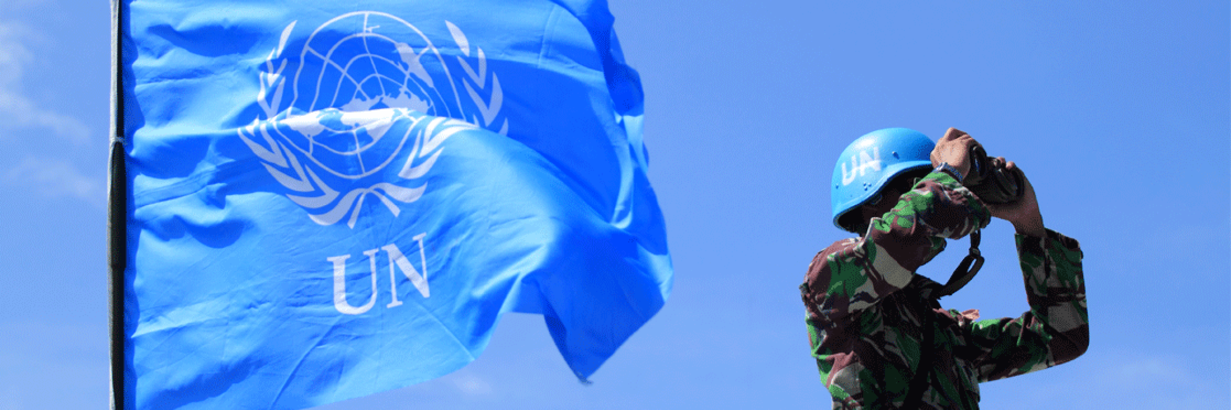 A person in camouflage next to a blue flag.