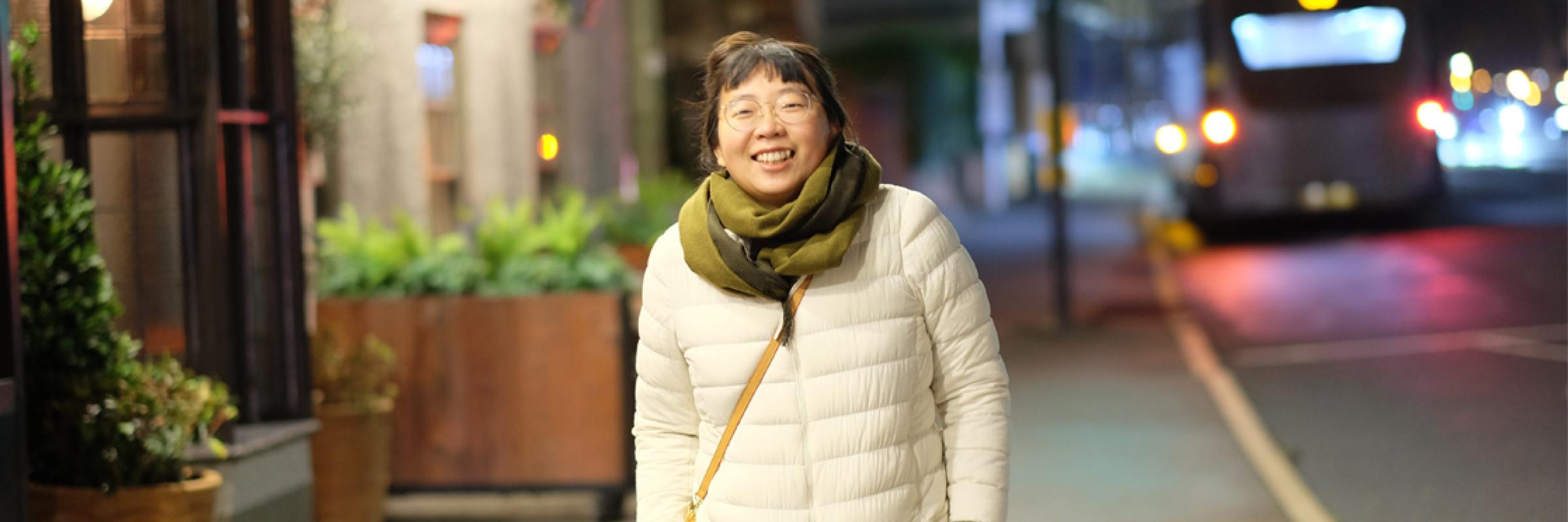 A person wearing a white coat and green scarf walking on a pavement