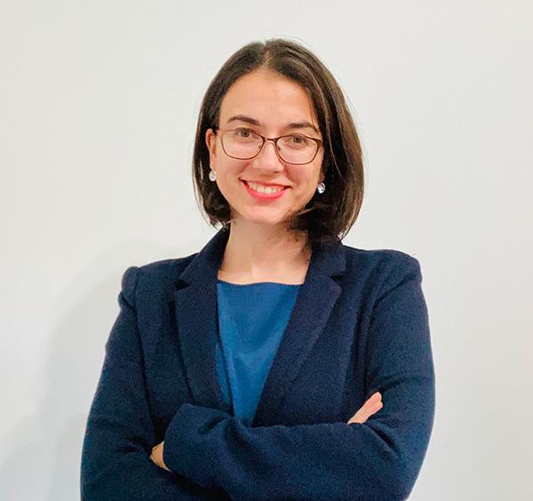 Image of a woman wearing glasses, a dark blue jacket and blue top smiling at camera