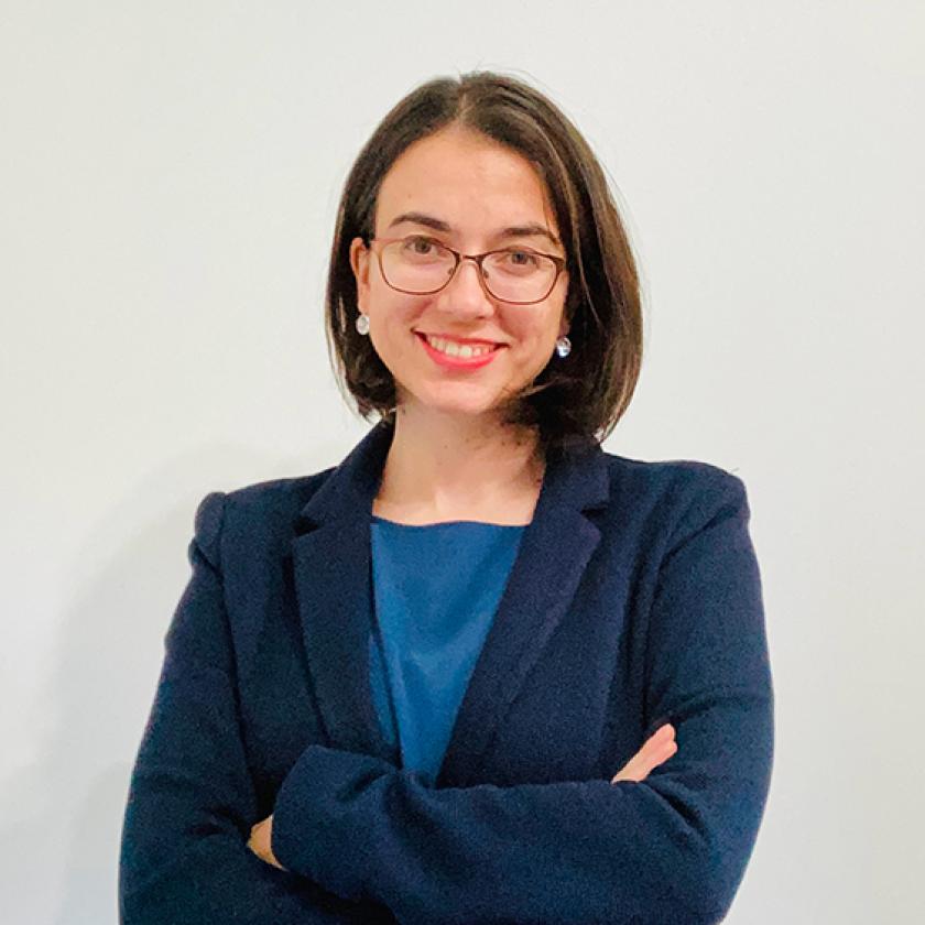 Image of a woman wearing glasses, a dark blue jacket and blue top smiling at camera