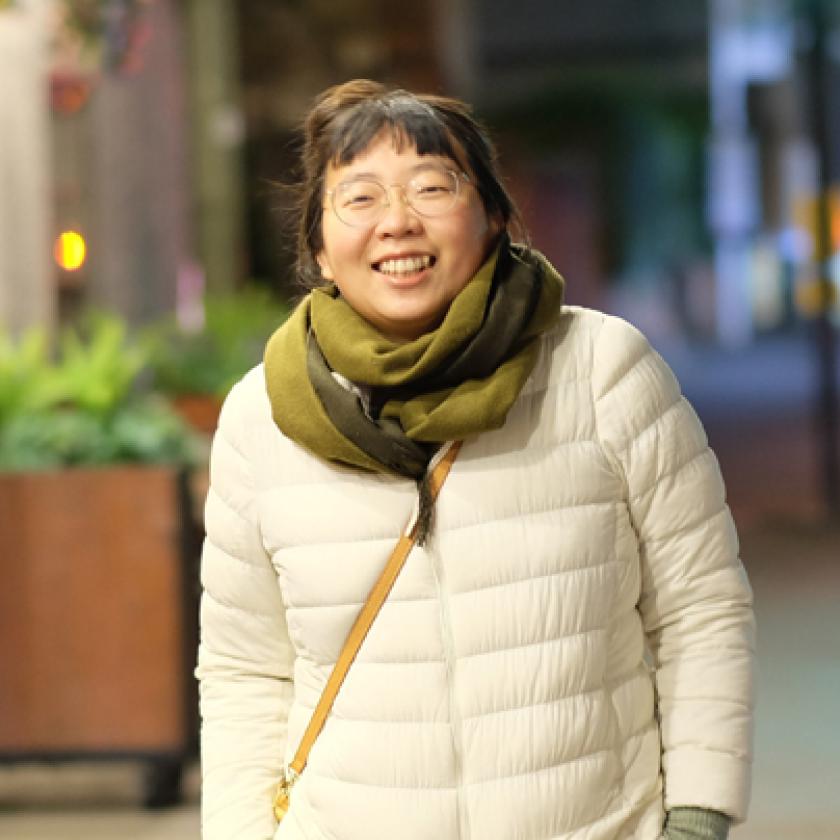 A person wearing a white coat and green scarf walking on a pavement